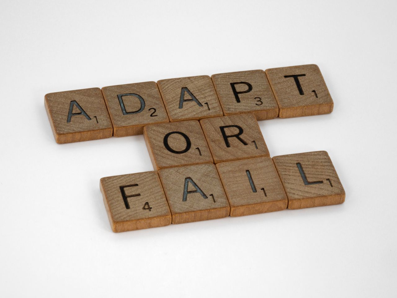 Offerings Scrabble tiles spell Adapt or Fail on a white background, conveying a motivational message.