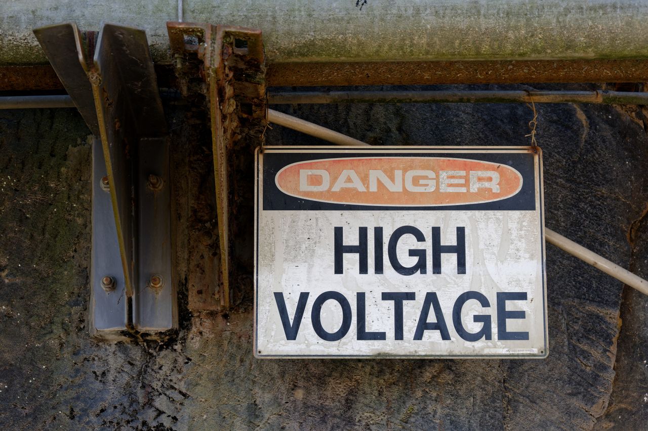 Rusty Danger High Voltage sign on an outdoor wall, indicating electrical hazard.
